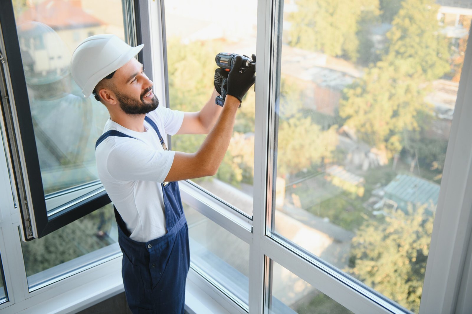 Workman in overalls installing or adjusting plastic windows in the living room at home.